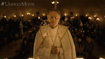 A Priest Is Praying In Front Of A Crowd With #Unholymovie Written On The Bottom Right GIF