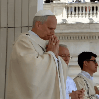 A Priest Is Praying With His Hands Folded In Front Of A Balcony GIF