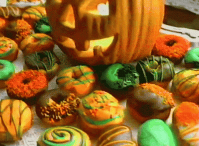 A Pumpkin With A Face Carved Into It Sits On Top Of A Pile Of Donuts GIF