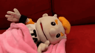 A Puppet Is Laying On A Couch With A Pink Blanket . GIF
