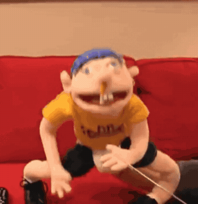 A Puppet Is Sitting On A Red Couch With A Stick In His Mouth . GIF