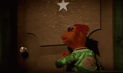 A Puppet Is Standing In Front Of A Door With A Star Above It GIF
