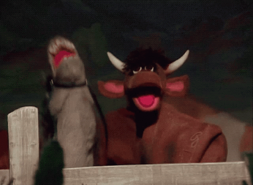 A Puppet Of A Cow With A Pink Tongue Looks Over A Fence GIF