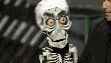 A Puppet Of A Skeleton Is Standing Next To A Man In A Suit . GIF