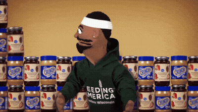 A Puppet Wearing A Green Shirt That Says Feeding America Stands In Front Of Jars Of Peanut Butter GIF
