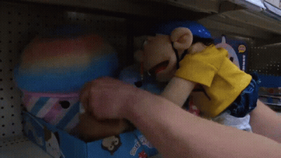 A Puppet With A Pencil In His Mouth Is Sitting On A Shelf In A Store .. GIF