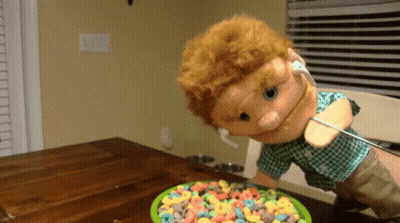A Puppet With Ear Buds And A Bowl Of Cereal GIF