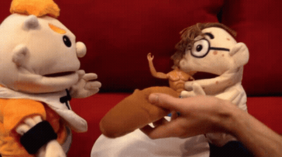 A Puppet With Glasses Is Being Held By Another Puppet On A Red Couch GIF