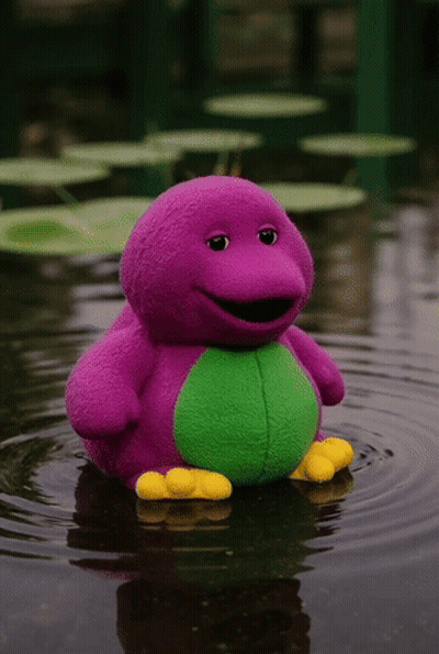 A Purple And Green Barney Stuffed Animal Is Floating In The Water GIF