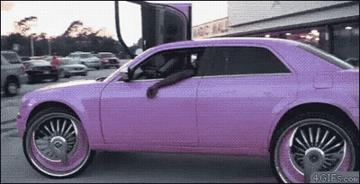 A Purple Car With Big Wheels Is Parked In A Lot GIF