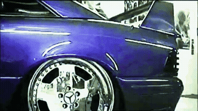 A Purple Car With Chrome Wheels And A Mercedes Logo On The Front GIF