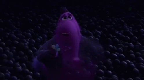 A Purple Cartoon Character Is Standing In A Pile Of Purple Balls In The Dark . GIF