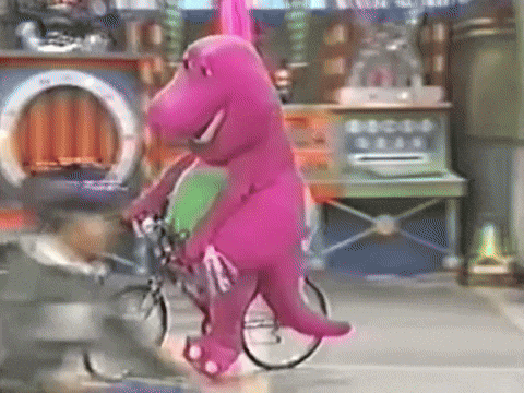 A Purple Dinosaur Is Riding A Bike On A City Street GIF