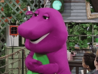 A Purple Dinosaur Is Standing In Front Of A Green Light And Smiling . GIF