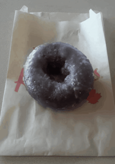 A Purple Donut Is Sitting On A White Paper Bag With The Letter A Printed On It GIF