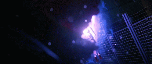 A Purple Light Is Shining Through A Fence In The Dark GIF