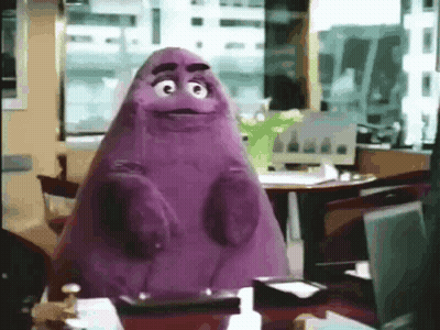 A Purple Mcdonald 'S Mascot Is Sitting At A Desk In An Office . GIF