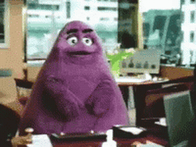 A Purple Monster Is Sitting At A Desk In An Office GIF