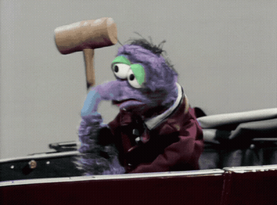 A Purple Stuffed Animal Is Holding A Wooden Mallet On Its Head GIF