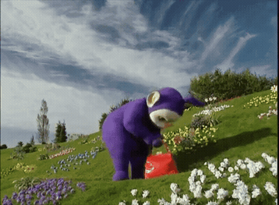 A Purple Teddy Bear Is Standing In A Field Of White Flowers GIF
