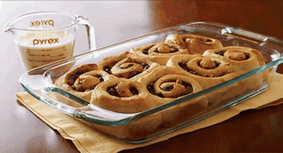 A Pyrex Measuring Cup Sits Next To A Casserole Dish Of Cinnamon Rolls GIF