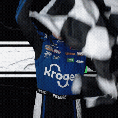 A Race Car Driver Wearing A Kroger Jersey Holds A Checkered Flag GIF