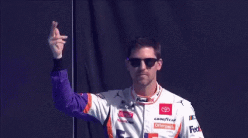 A Race Car Driver Wearing Sunglasses And A Fedex Shirt Is Waving His Hand . GIF