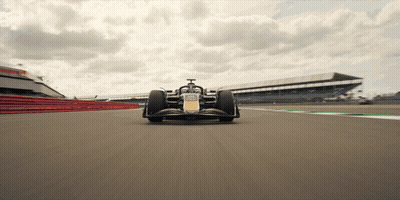 A Race Car Is Driving Down A Track With A Large Building In The Background GIF
