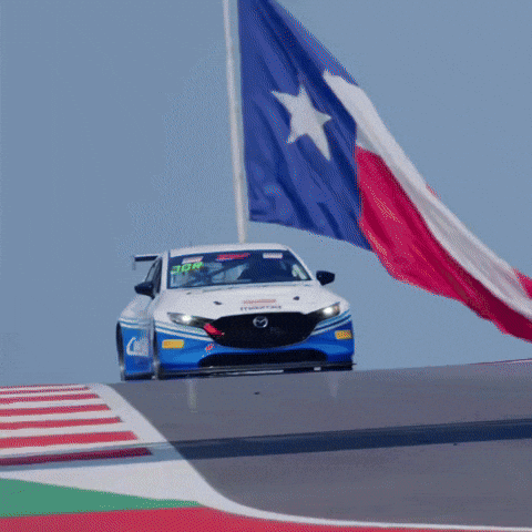 A Race Car Is Driving Down A Track With A Texas Flag Flying In The Background GIF