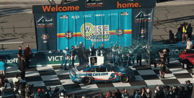 A Race Car Is On A Checkered Race Track With A Banner That Says Welcome Home GIF