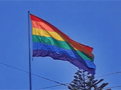 A Rainbow Flag Is Flying In A Blue Sky GIF