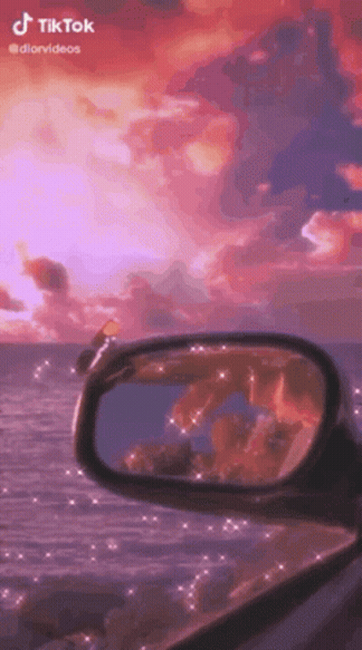 A Rear View Mirror Of A Car With A Sunset In The Background . GIF