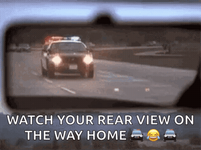 A Rear View Mirror Shows A Police Car Driving Down A Road GIF