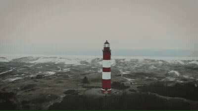 A Red And White Lighthouse Sits On Top Of A Hill GIF