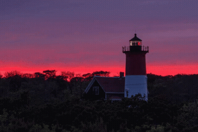 A Red And White Lighthouse Stands In Front Of A Sunset Sky GIF