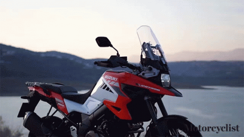 A Red And White Suzuki Motorcycle Is Parked Near A Lake GIF