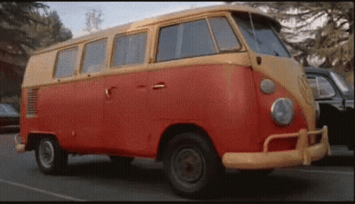 A Red And Yellow Van Is Parked On The Side Of A Road . GIF