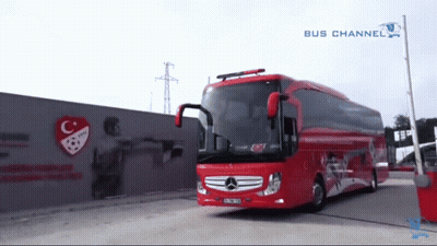 A Red Bus Is Parked In Front Of A Wall With A C And A Soccer Ball On It GIF