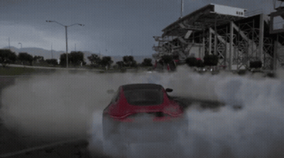 A Red Car Is Drifting In A Parking Lot With Smoke Coming Out Of The Tires GIF
