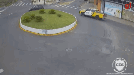 A Red Car Is Driving Around A Roundabout With A Yellow Truck Behind It . GIF