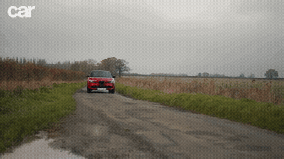 A Red Car Is Driving Down A Dirt Road With Car Written On The Bottom Right GIF