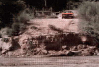 A Red Car Is Driving Down A Dirt Road With Trees In The Background GIF