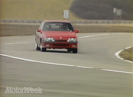 A Red Car Is Driving Down A Road With Motorweek Written On The Bottom Of The Screen GIF