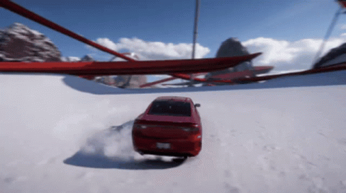 A Red Car Is Driving Down A Snowy Road With Mountains In The Background GIF