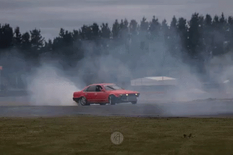 A Red Car Is Driving On A Track With Smoke Coming Out Of It GIF