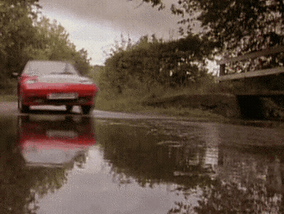 A Red Car Is Driving Through A Puddle On A Wet Road GIF