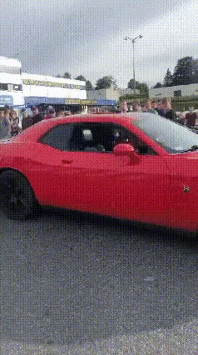 A Red Car Is Parked In A Parking Lot With A Crowd Of People Watching . GIF