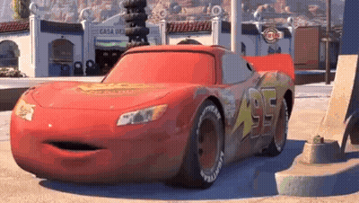 A Red Cartoon Car With A Big Mouth Is Parked On The Side Of The Road In Front Of A Building . GIF