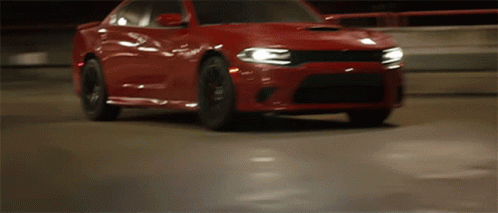 A Red Dodge Charger Is Driving Down A Road At Night GIF