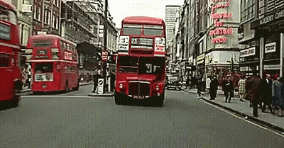 A Red Double Decker Bus Is Driving Down A Street GIF